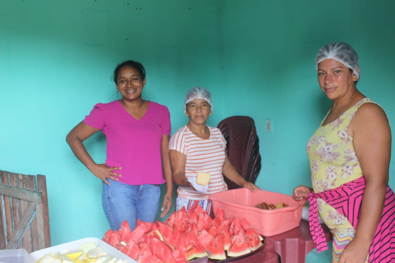 Simone à direita na foto, uma mesa com frutas e as colegas de grupo Maria e Antônia, respectivamente, do projeto “Horta para Cozinha” servindo lanches na comunidade de Piquiá de Baixo